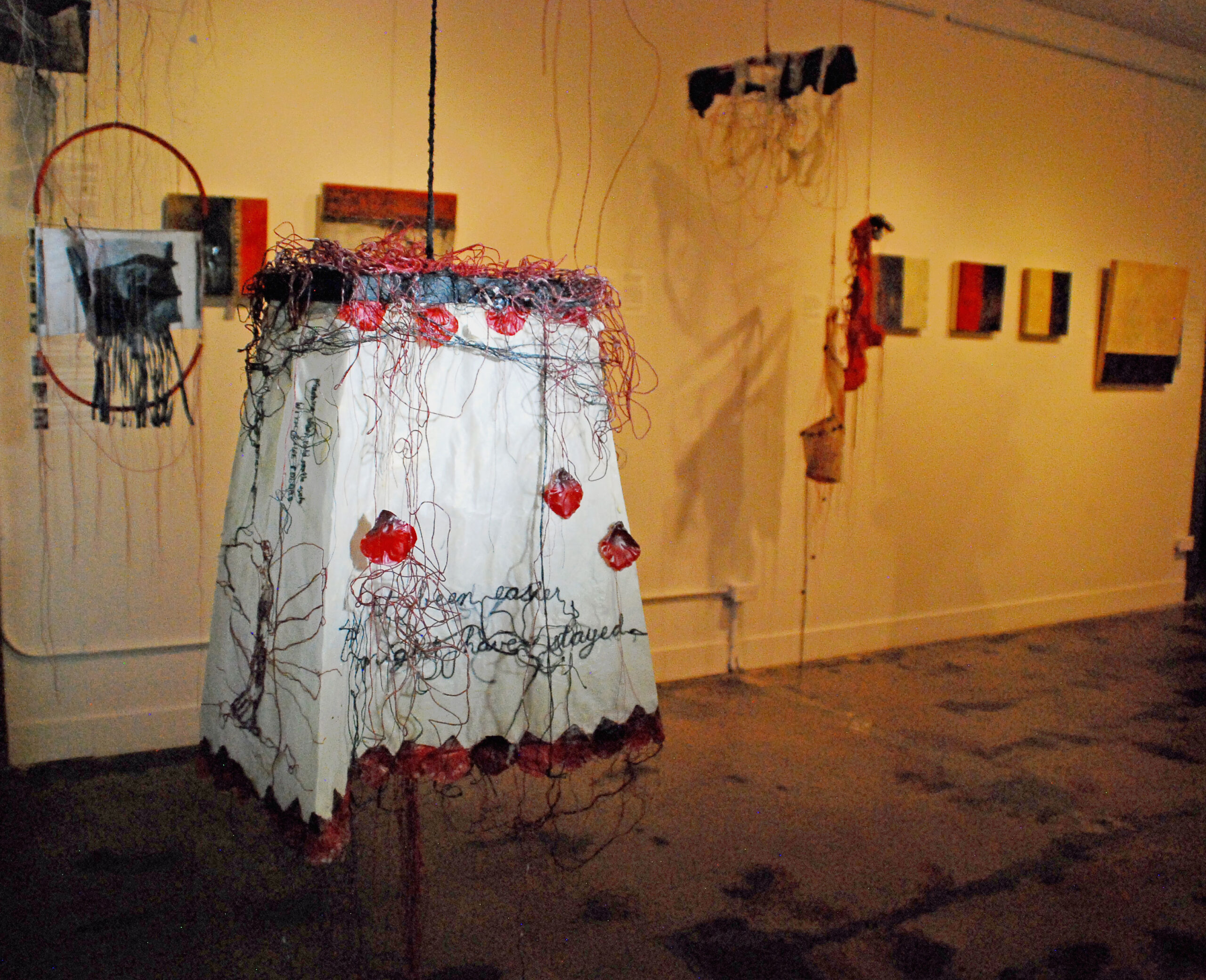 GO OR STAY?  A discarded woman’s skirt morphs into a lampshade-like four-sided suspended sculpture. Hand-embroidered cursive on opposing sides reflects the dilemma faced by migrants who must make heart-wrenching choices between staying in the homeland they love versus facing the dangers of crossing borders to seek physical safety or a viable livelihood for their family. A reminder that people do not just pick up and abandon the place they’ve lived for generations without cause. Small print embroidery at the top repeats the clothing label “Made in Bangladesh” in English and Spanish, emblematic of the juxtaposition between Fast Fashion’s makers and consumers.
